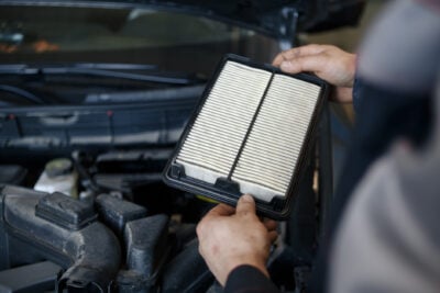 person holding an auto air filter in front of a car engine