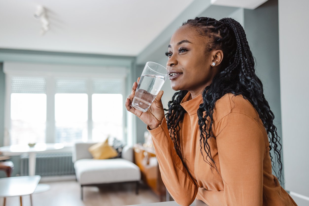 Young woman drinking water at home considering the sate of her water quality