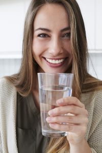 you woman smiling with a glass of filtered water from the fridge