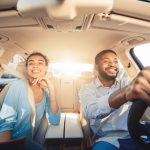 Enjoying travel. Excited african couple driving car and smiling, copy space