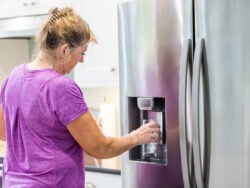 A woman is filling a glass with filtered water from a refrigerator