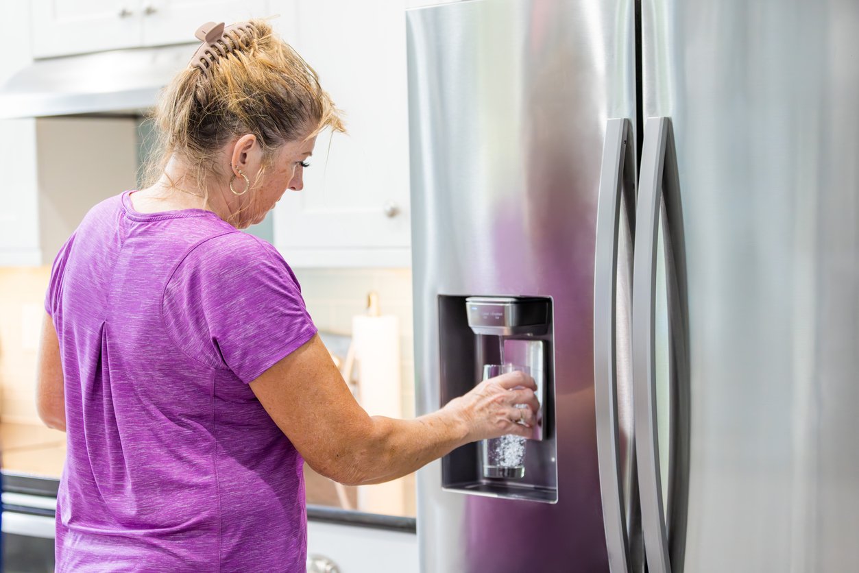 A woman is filling a glass with filtered water from a refrigerator