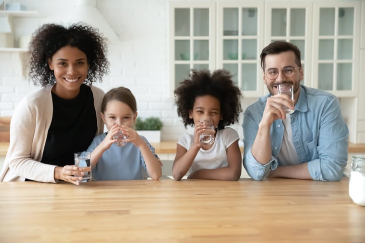 Portrait of happy young family with little kids drinking pure clean mineral water at home, smiling parents with small daughters children recommend healthy lifestyle.