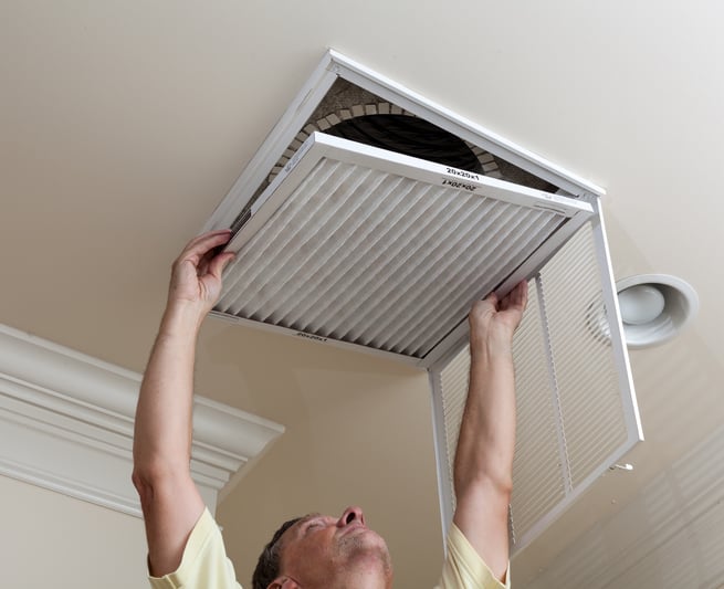 man changing air filter in ceiling