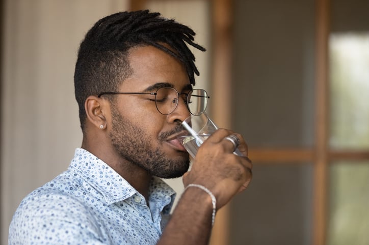 man wearing glasses enjoying fresh pure mineral water with closed eyes, holding glass, healthy lifestyle and good daily habit concept, body and skin care