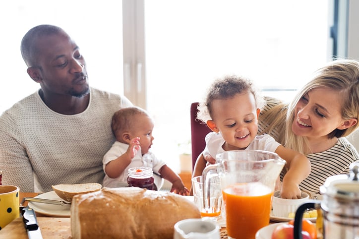 Beautiful young family at home with their cute daughter and little baby son having breakfast together.
