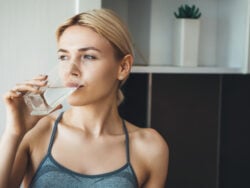 Young fitness lady drinking water after yoga exercises wearing sportswear at home in the kitchen