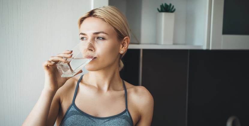 Young fitness lady drinking distilled water after yoga exercises wearing sportswear at home in the kitchen