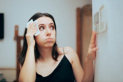woman who is hot adjusting thermostat in home