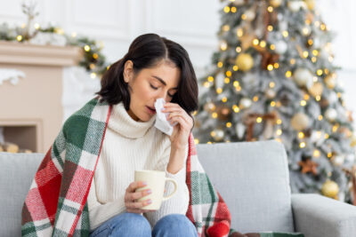 woman wiping nose with lit Christmas tree in background. Illustrating the right time to change air filter is after the holidays.