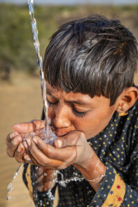 Indian young boy is drinking fresh water, desert village, Thar Desert, Rajasthan, India. Potable water is very precious on the desert - Rajasthani women and children often walk long distances through the desert to bring back jugs of water that they carry on their heads.